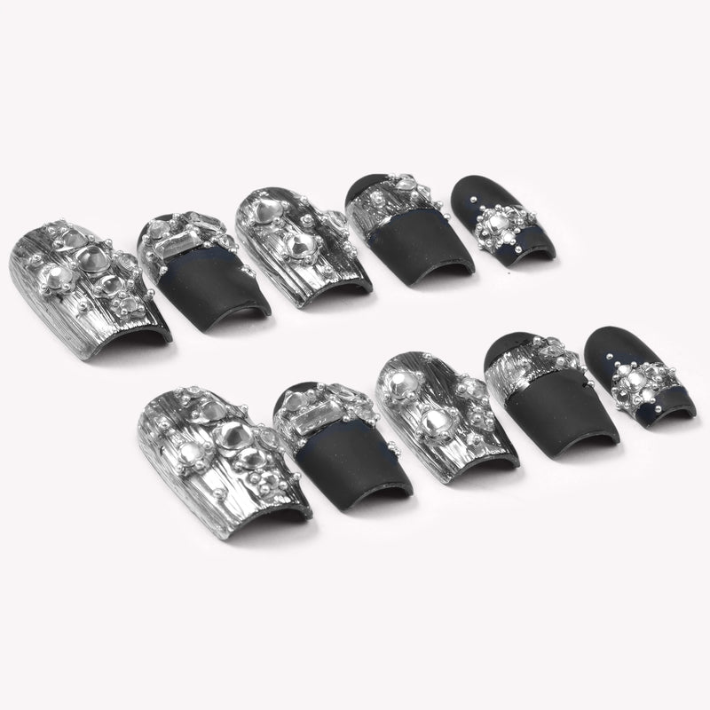 Flat lay of Noir Eclat press-on nail swatches with black bases, silver metallic accents, and pearl details