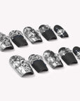 Flat lay of Noir Eclat press-on nail swatches with black bases, silver metallic accents, and pearl details