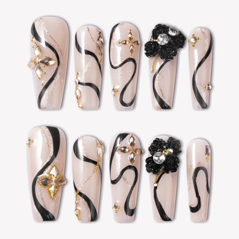 Flat lay of beige press-on nails with black swirls, gold accents, and floral embellishments.
