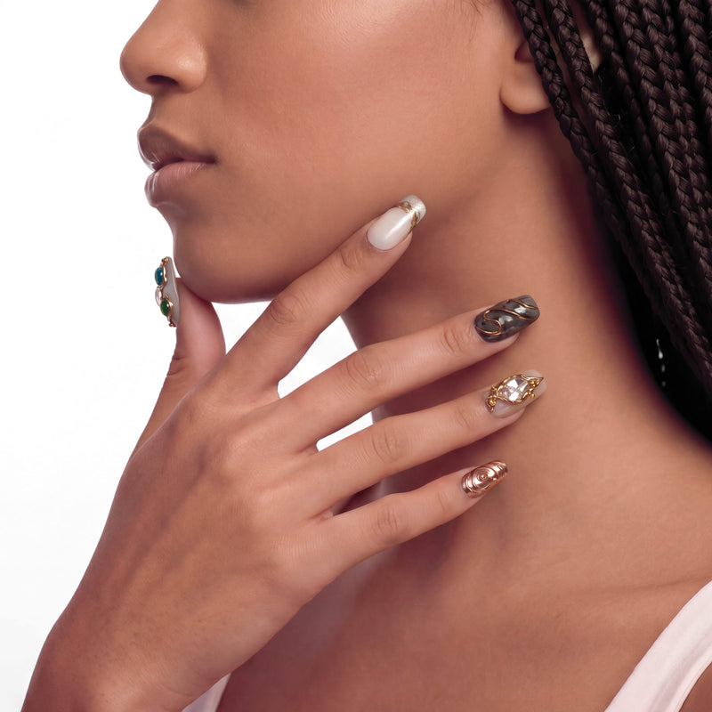 Side profile of a hand model wearing pearl white and gold press-on nails with ornate jewel accents.