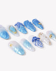 Angled flat lay of Ocean Rhapsody blue and pearl press-on nails with jellyfish, starfish, shells and waves
