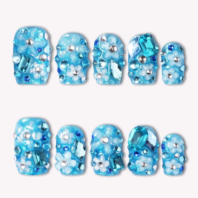 Flat lay of Ocean Sparkle Bloom handmade press-on nails with blue glitter, crystals, floral accents, and silver beads.
