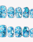 Flat lay of Ocean Sparkle Bloom handmade press-on nails with blue glitter, crystals, floral accents, and silver beads.