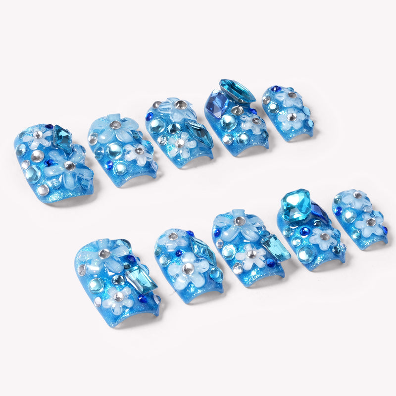 Flat lay of blue Ocean Sparkle Bloom handmade press-on nails with floral accents, crystals, and silver beads.