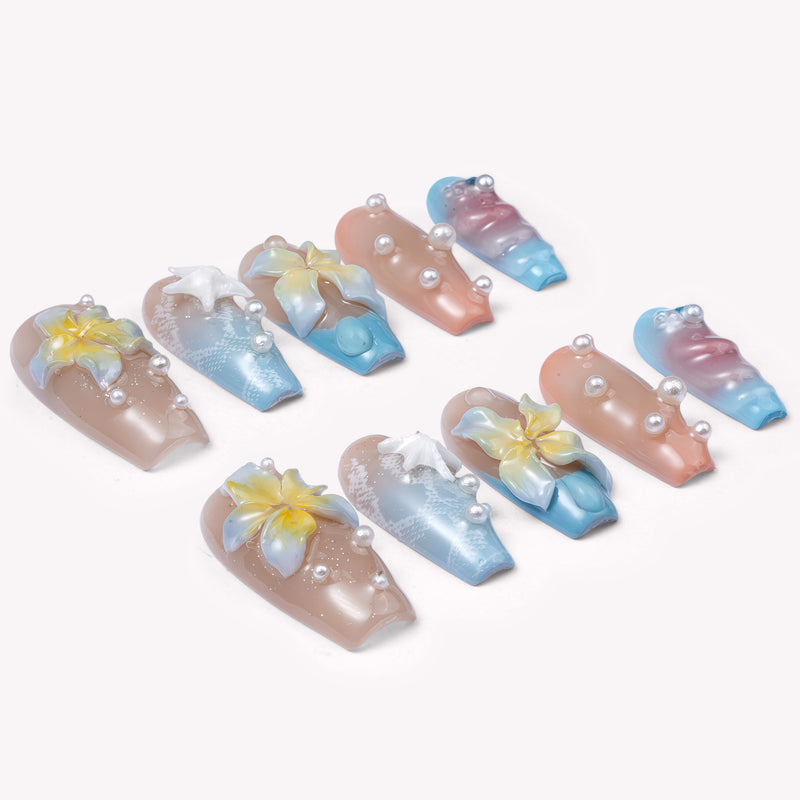 A flat lay of beach-inspired press-on nails with yellow flowers, starfish accents, and pearl details on a white background