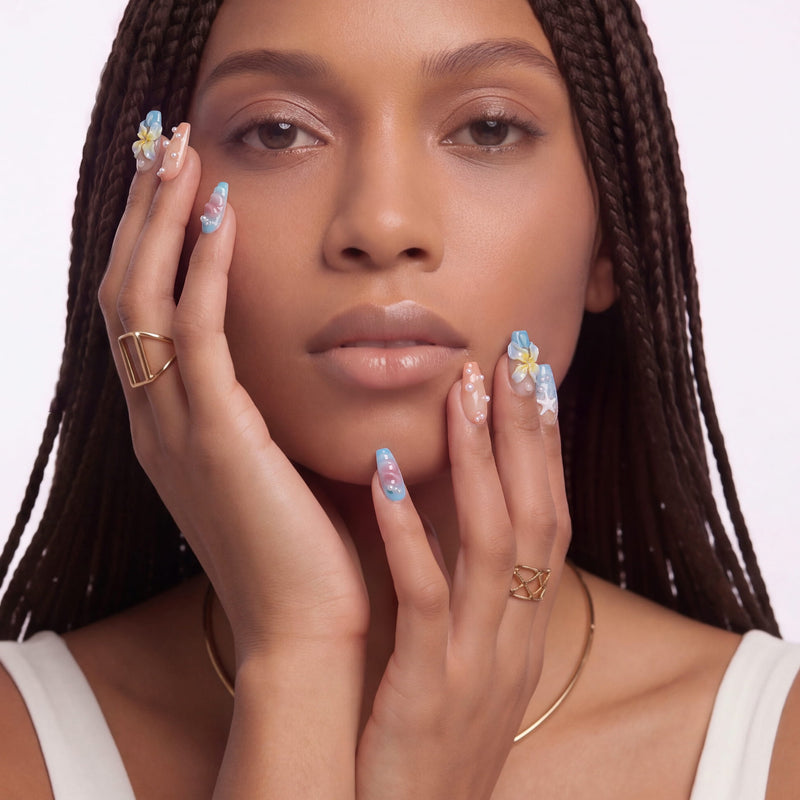 A front-facing hand model wearing blue floral press-on nails with pearl and star accents