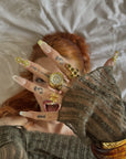 Face close-up hand model wearing Opal Dynasty press-on nails with nude pink bases, gold crown accents, pearl flowers, rhinestones, and rings