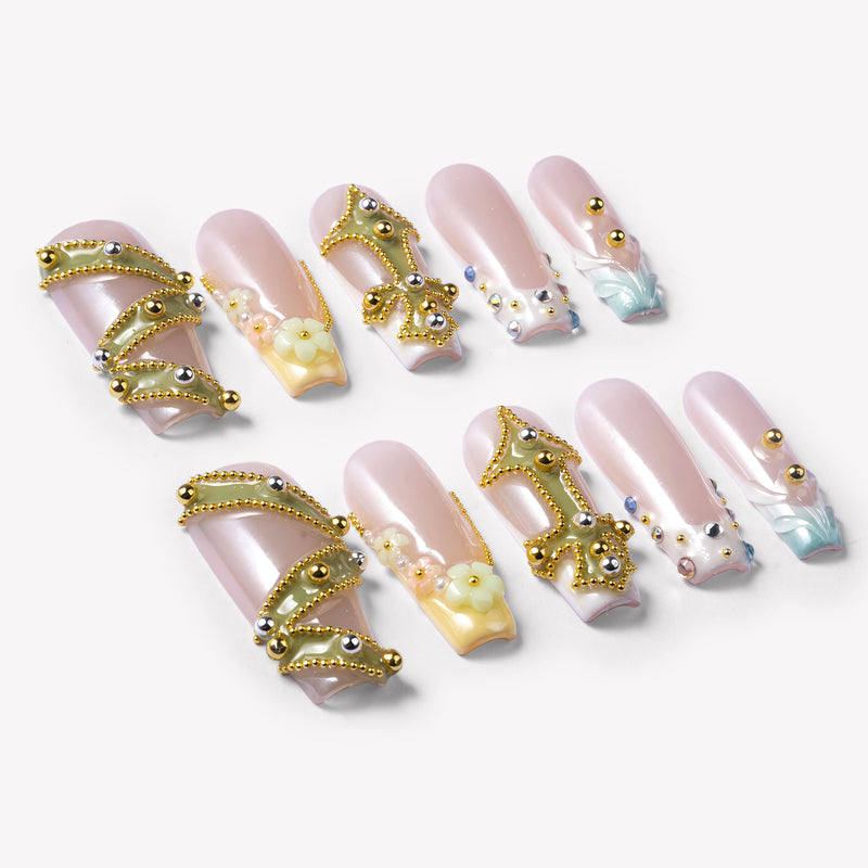 Flat lay of Opal Dynasty press-on nails with nude pink bases, gold crown details, pearl flowers, rhinestones, and blue translucent accents