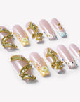 Flat lay of Opal Dynasty press-on nails with nude pink bases, gold crown details, pearl flowers, rhinestones, and blue translucent accents