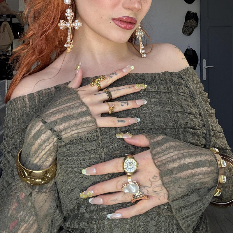 Hand model wearing Opal Dynasty press-on nails with nude pink bases, gold crown details, pearl accents, rhinestones, and layered gold jewelry