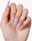 Hand model wearing Opal Whisper press-on nails in pale pink and clear shimmer with white flower accents