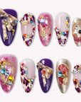 Opulent Ribbon Reverie press-on nails in purple pink and ivory with gold ribbon details and colorful gem accents arranged on a white background