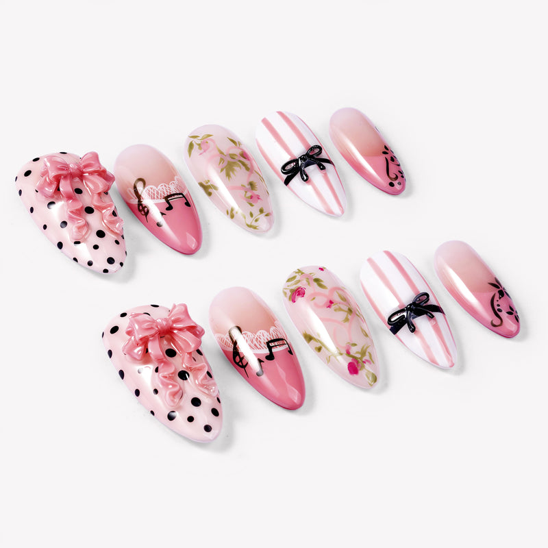 Angled flat lay of Parisian Charm press-on nails with pink bows, black polka dots, lace, floral vines, and striped bow art