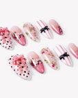 Angled flat lay of Parisian Charm press-on nails with pink bows, black polka dots, lace, floral vines, and striped bow art