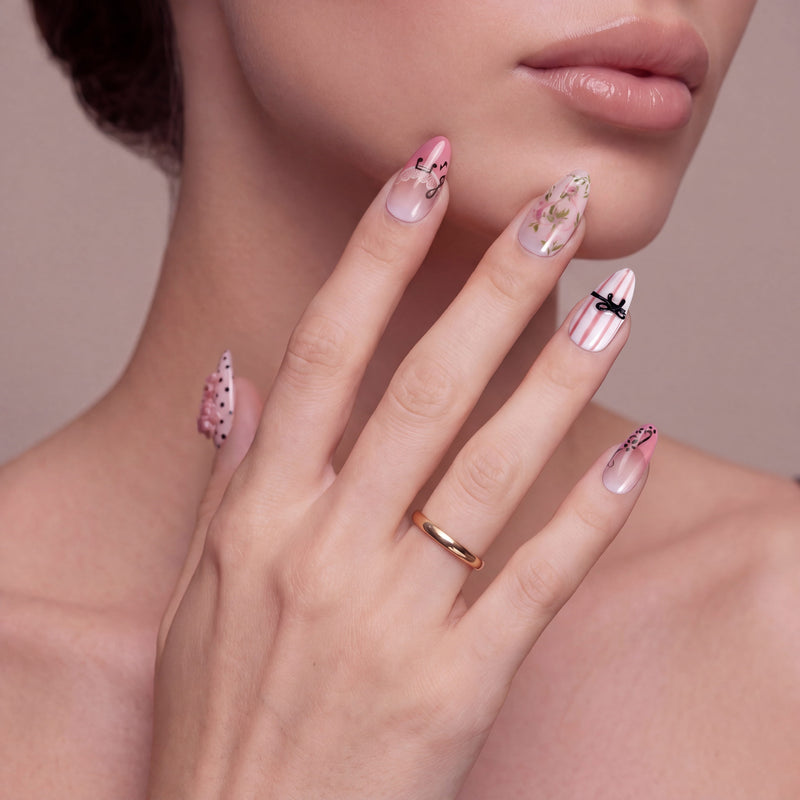 Face hand model wearing Parisian Charm press-on nails with pink lace, floral art, striped bow detail, and black polka dots