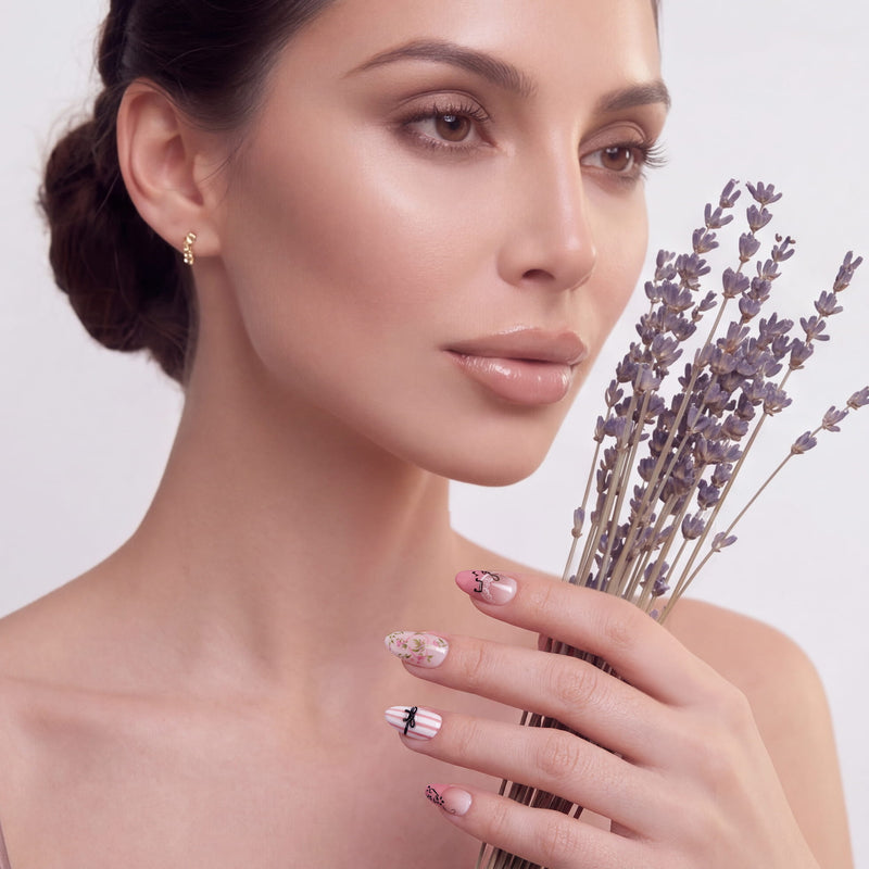 Hand model holding lavender while wearing Parisian Charm press-on nails with floral art, pink stripes, lace, and bow details