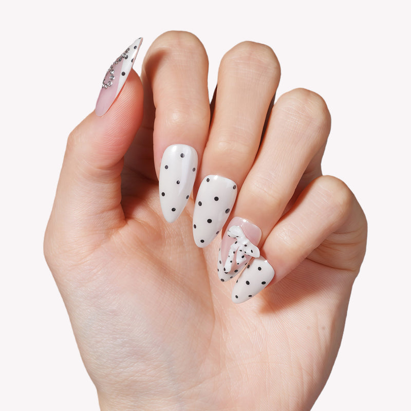 Close-up of a hand model wearing Parisian Polka press-on nails in ivory and blush with black polka dots and pearl accents