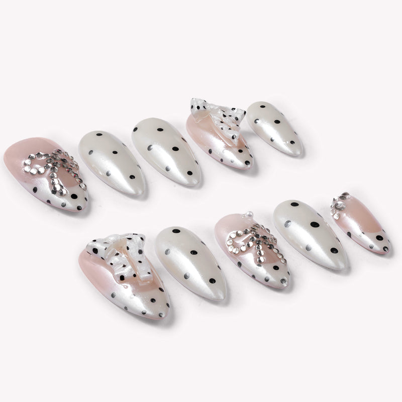 Parisian Polka press-on nail set in ivory and blush with black polka dots and pearl chain accents arranged in a flat lay on a white background