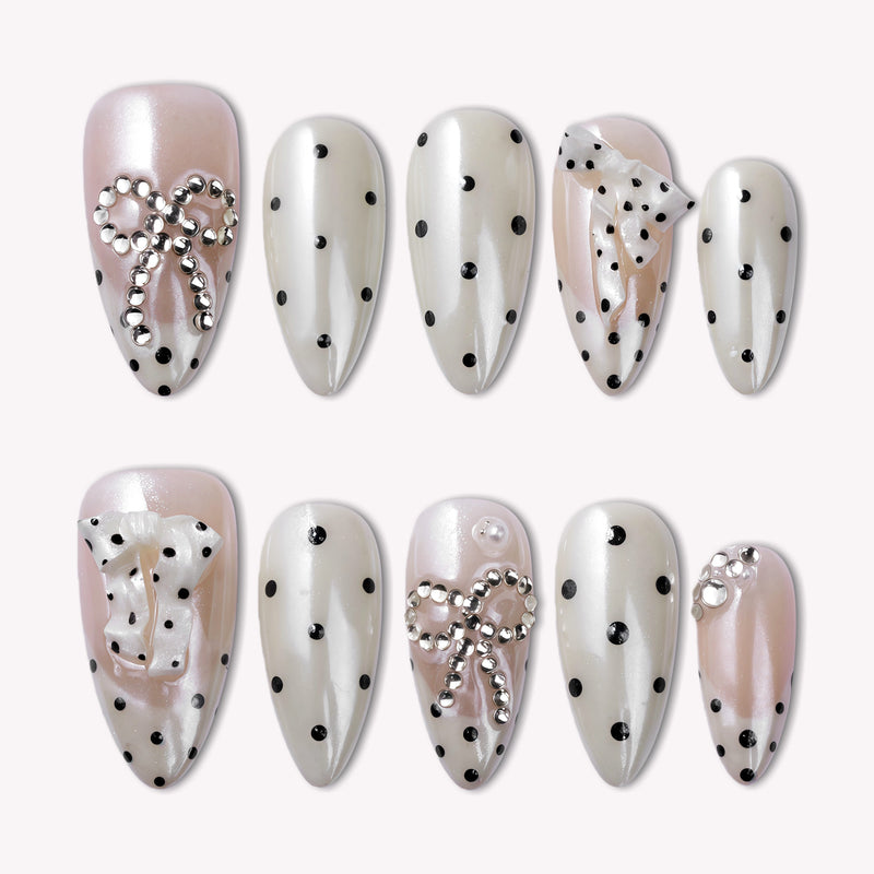 Parisian Polka press-on nail set in ivory and blush with black polka dots and pearl chain accents arranged on a white background