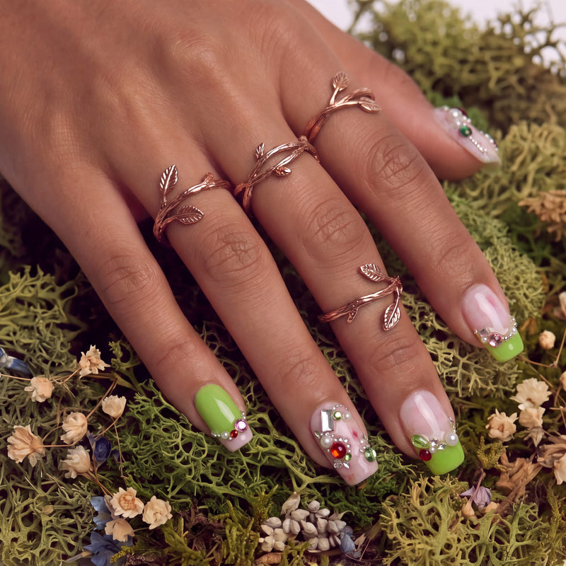 Pastel Dream handmade press-on nails worn in a close-up hand pose on moss with lime green tips and jeweled accents