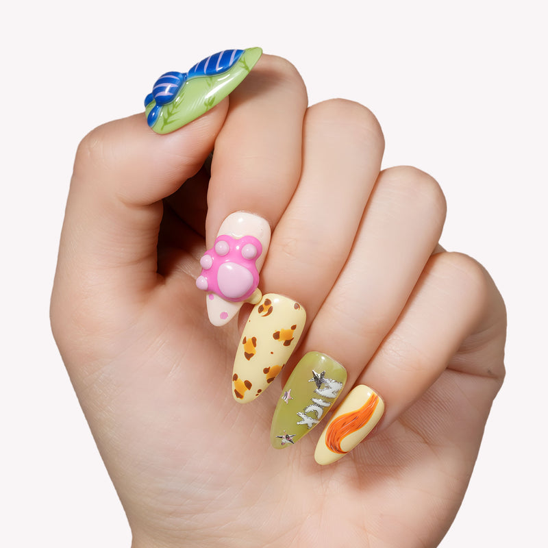 Hand model wearing cartoon-themed press-on nails with blue, green, pink, and yellow character-inspired accents