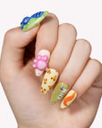 Hand model wearing cartoon-themed press-on nails with blue, green, pink, and yellow character-inspired accents