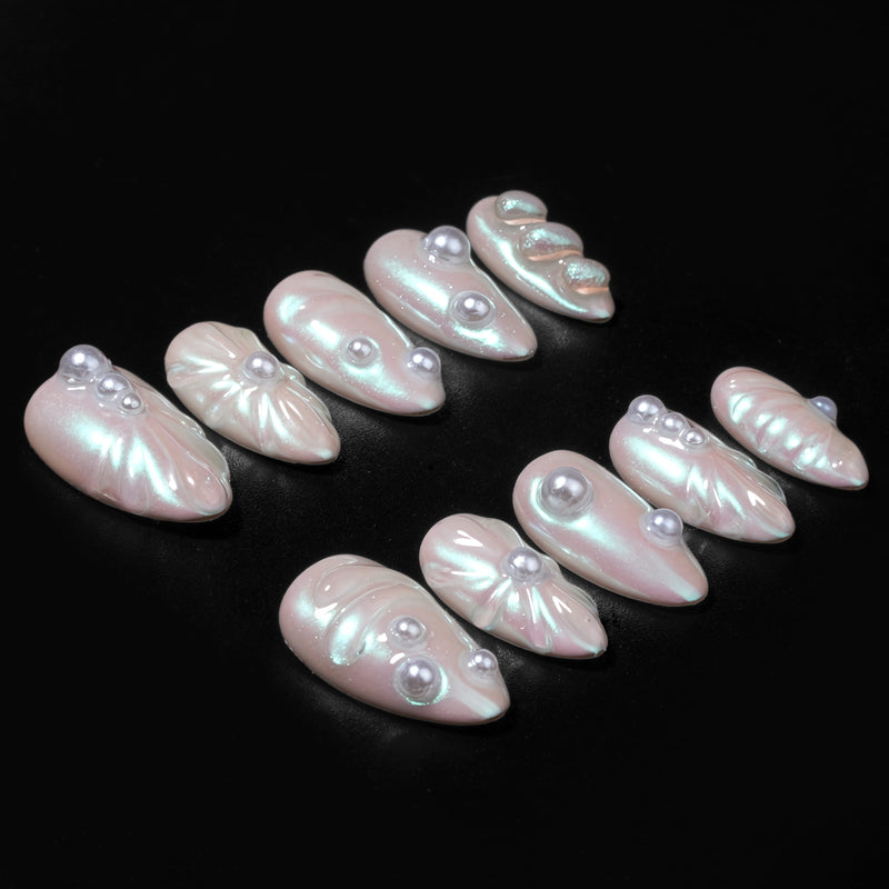 Pale blush pearlescent press-on nails with pearl accents arranged on a black background.