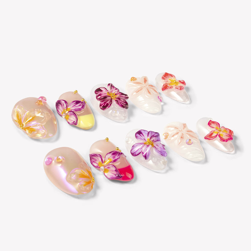 Angled flat lay of Petal Poem colorful press-on nails with sculpted purple, pink, peach and yellow flowers