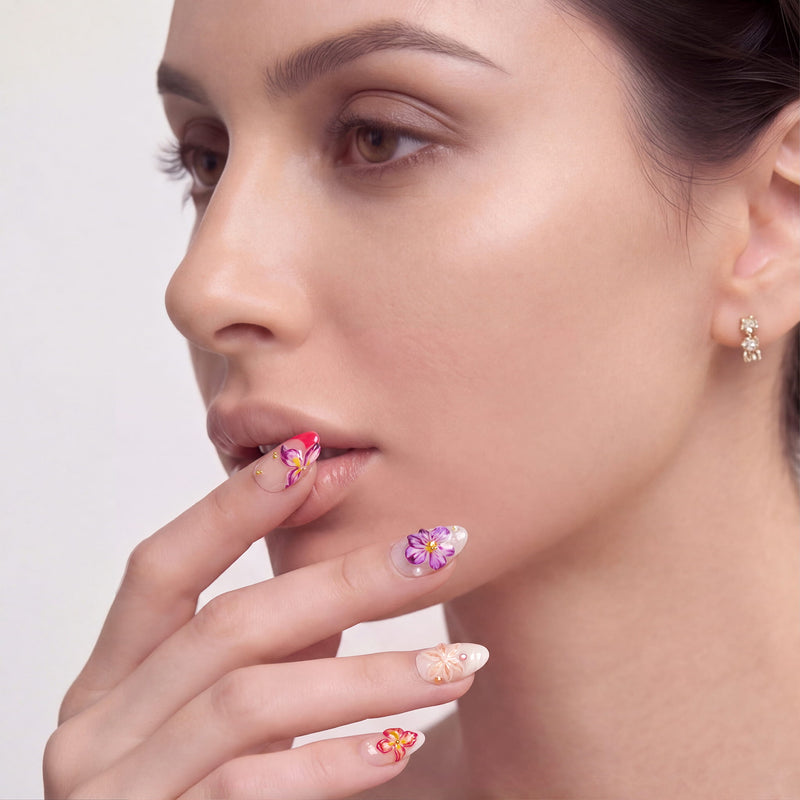 Model wearing Petal Poem colorful floral press-on nails with pink, purple and peach flower designs near her face