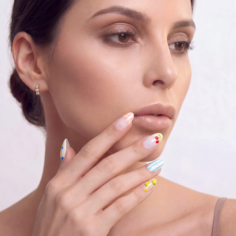 Face close-up of a hand model wearing handmade press-on nails with blue stripes and fruit accents.