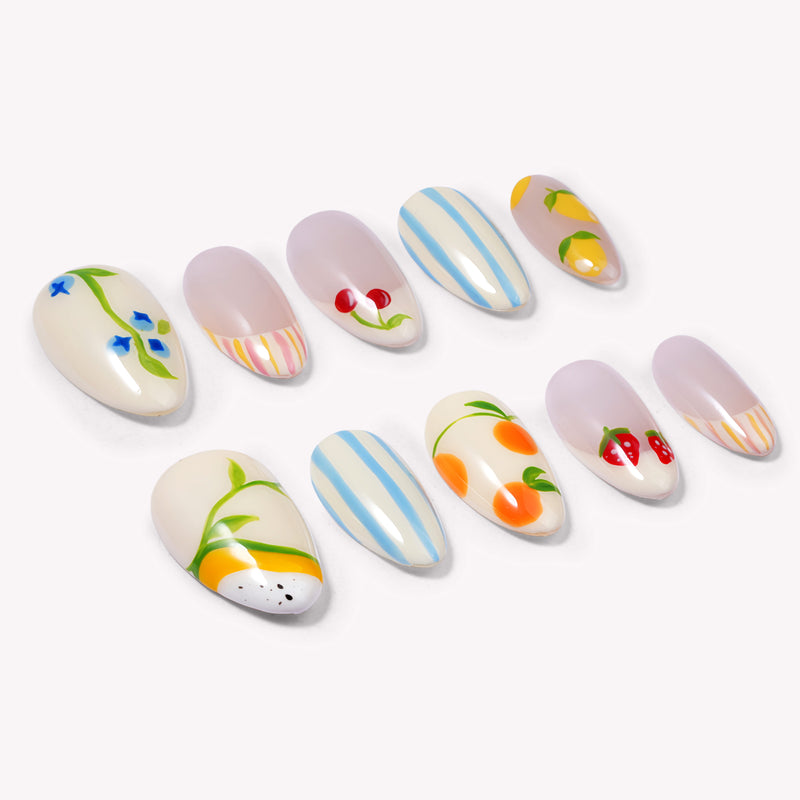 Set of handmade press-on nails with blue stripes, cherries, lemons, strawberries, and peach designs on a white flat lay.