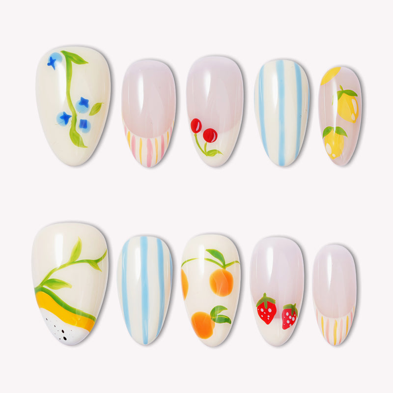 Set of handmade press-on nails with fruit and floral designs, blue stripes, and pastel accents on a white flat lay.
