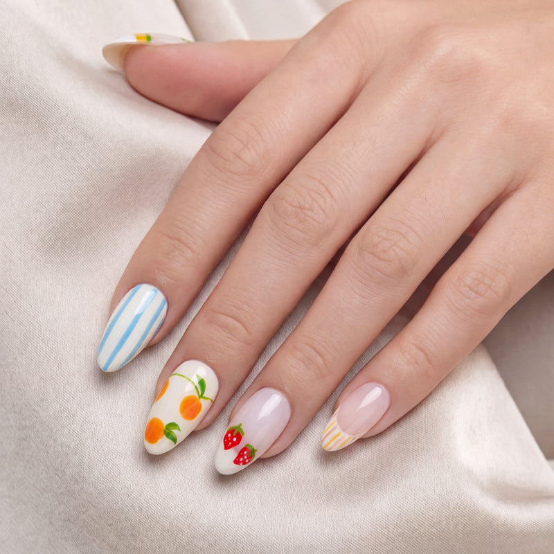 Hand model wearing handmade press-on nails with blue stripes, orange fruit, strawberry, and pastel accent designs.