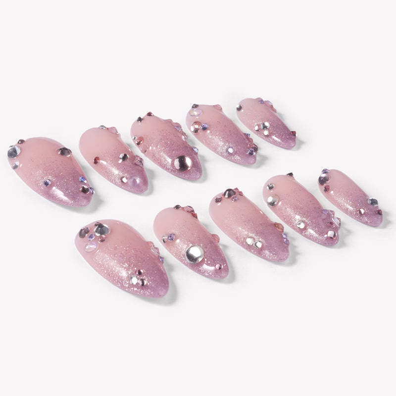 Angled flat lay of Pink Fairy Dust press-on nails with soft pink shimmer, glittery cat-eye tips, and rhinestone accents