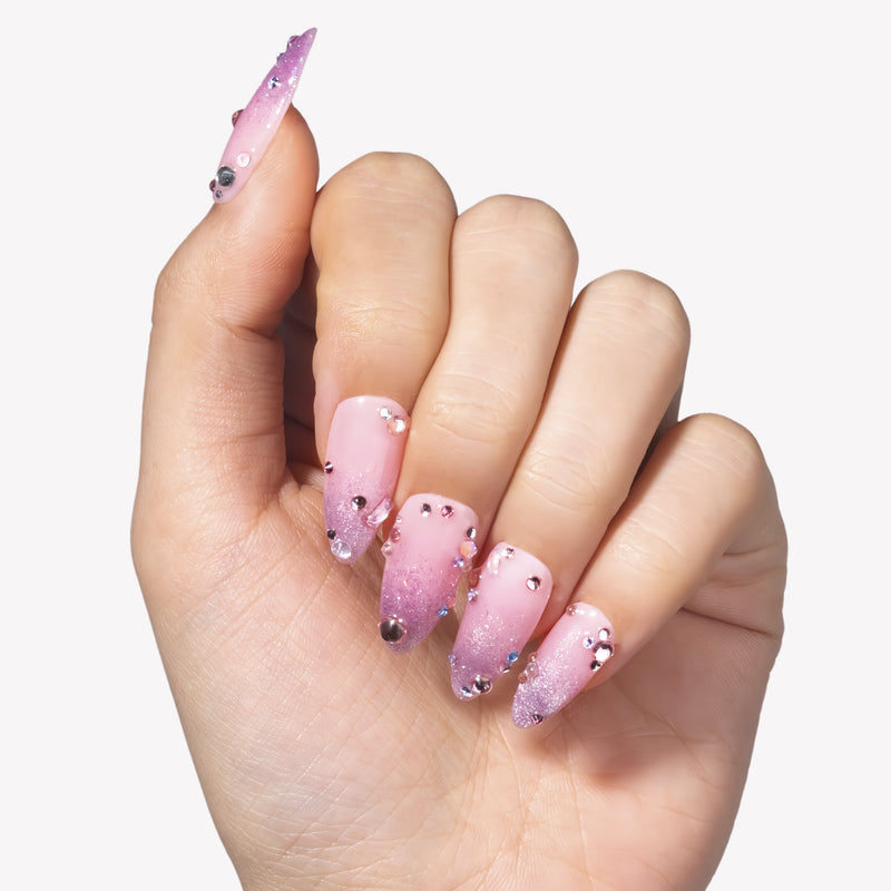 Hand model wearing Pink Fairy Dust press-on nails with pink shimmer gradients, cat-eye sparkle, and rhinestone accents