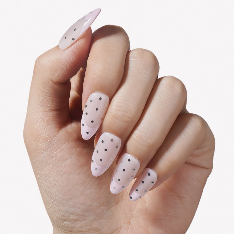 Hand model wearing blush pink press-on nails with black and silver polka dots