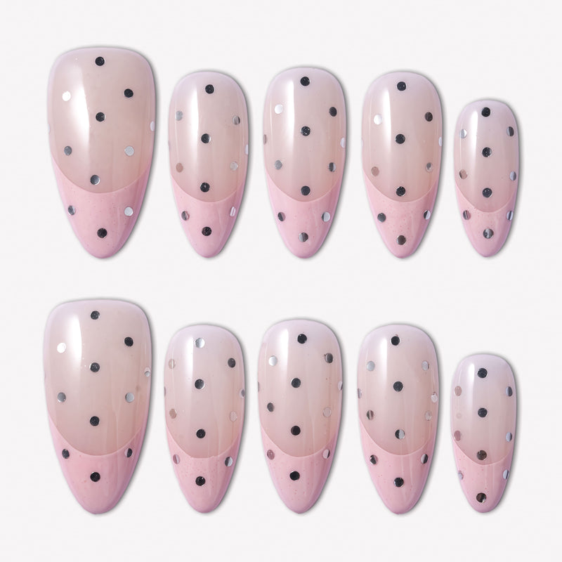 Flat lay of blush pink and beige press-on nails with black and silver polka dots in rounded oval shapes