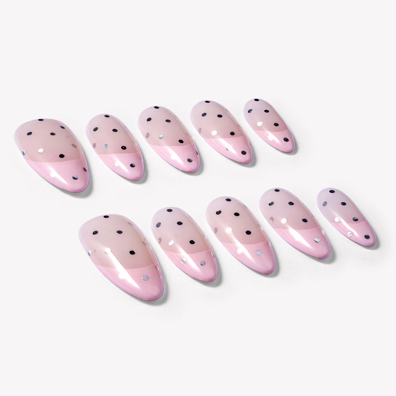 Flat lay of blush pink press-on nails with black polka dots and glossy pink French tips