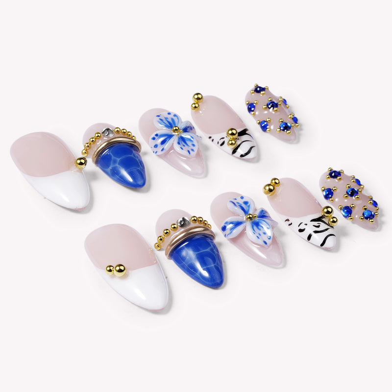 Flat lay of Porcelain Azure handmade press-on nails with cobalt blue, white, nude, floral, and gold bead accents.
