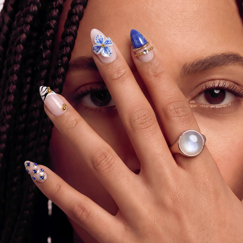 Hand model wearing Porcelain Azure handmade press-on nails with blue floral accents, gold beads, and a cobalt blue accent nail.