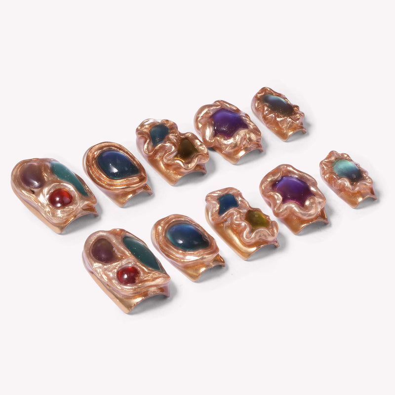 Flat lay of sculptural multicolor gemstone press-on nails with gold settings on a white background.