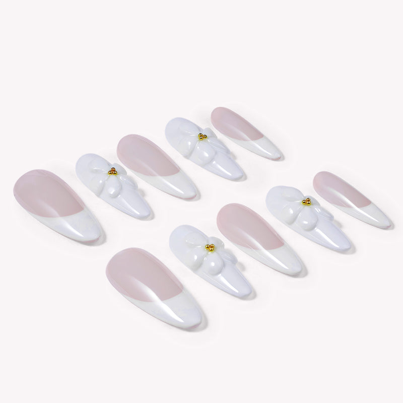 Diagonal flat lay of pale pink and white almond press-on nails with 3D white flower accents and gold centers on a white background.