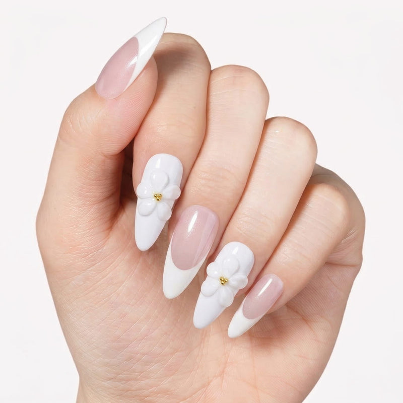 Hand model wearing pale pink and white almond press-on nails with 3D white flower accents and gold centers.