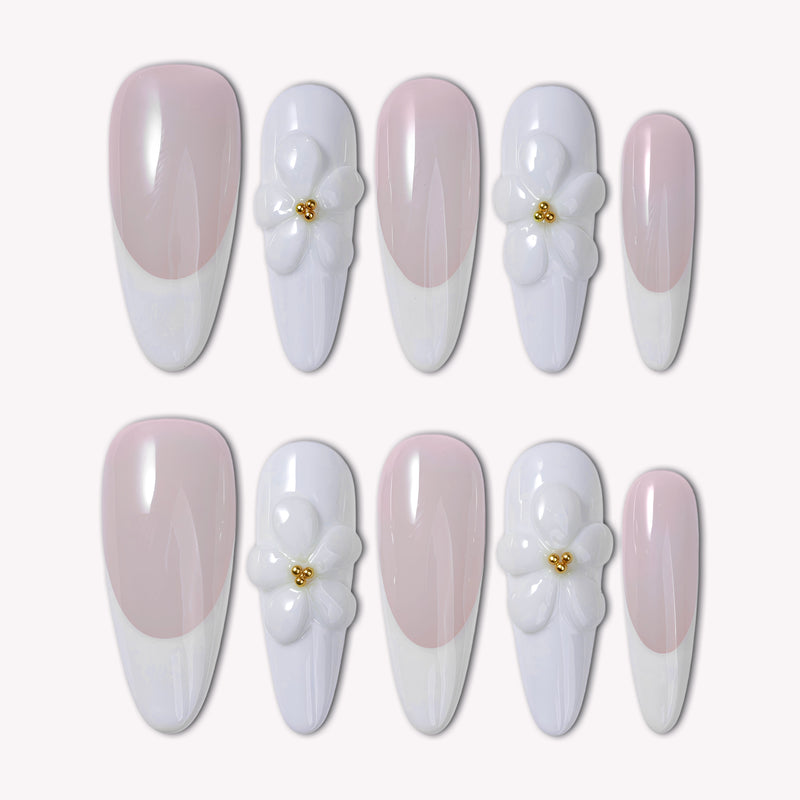 Flat lay of pale pink and white almond press-on nails with 3D white flower accents and gold centers on a white background.