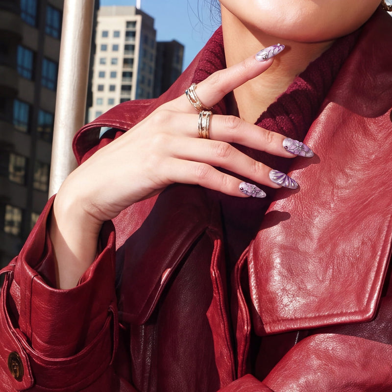 Model wearing Purple Dream lavender floral press-on nails with silver rings and a red leather jacket