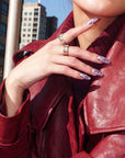 Model wearing Purple Dream lavender floral press-on nails with silver rings and a red leather jacket