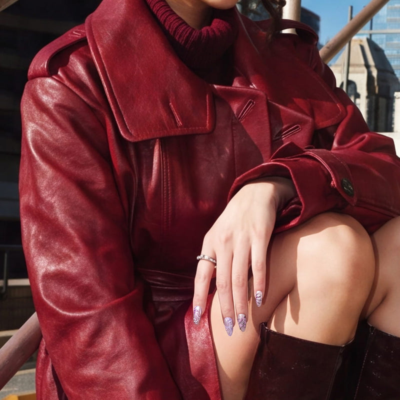 Seated lifestyle photo of Purple Dream lavender floral press-on nails styled with a red leather coat