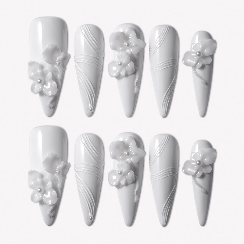 Quiet Sculpture press-on nails with glossy white long stiletto shapes, raised 3D flowers, pearl accents, and delicate sculpted line textures