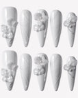 Quiet Sculpture press-on nails with glossy white long stiletto shapes, raised 3D flowers, pearl accents, and delicate sculpted line textures