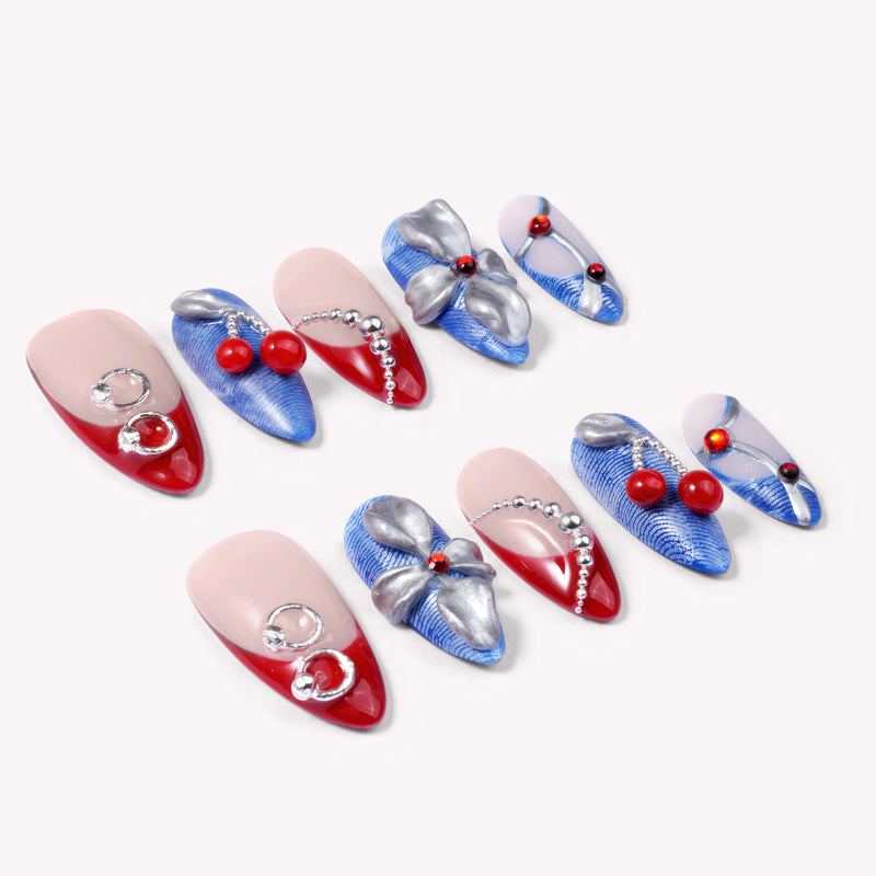 Rebel Cherry handmade press-on nails flat lay showing red tips, blue textured nails, silver bows, and cherry charms